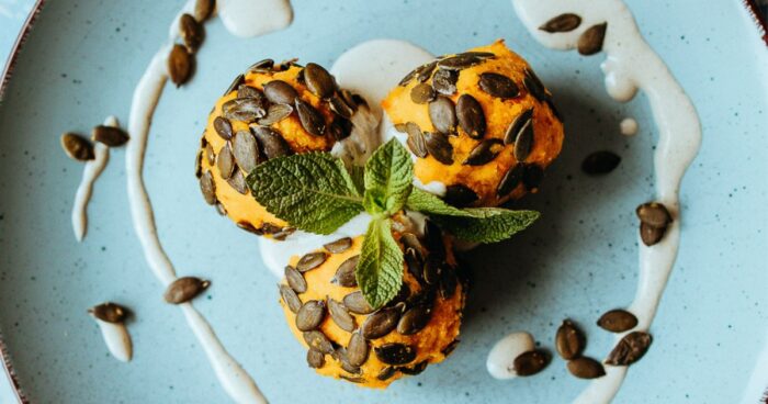 Hotové domácí slané dýňové kuličky posypte dýňovými semínka a mlsejte je s jogurtem.