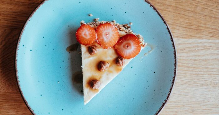 Ozdobte cheesecake plátky čerstvých jahod, které přidají svěžest a barvu, doplněné o křupavost nasekaných lískových ořechů, které zaručí harmonii textur a bohatou oříškovou chuť.